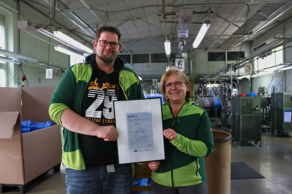 Zwei Mitarbeiter von PAPUREX, ein Mann links und eine Frau rechts, halten gemeinsam das neue ISO 9001 Zertifikat