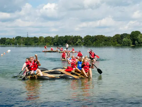 Drei Flöße mit einigen Personen, die rote Schwimmwesten tragen auf einem See bei einem Teambuilding Event