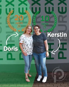 Stelln_in_Mörlenbach_Doris_Kerstin Zwei Frauen, vor einer weißen Wand mit der Aufschrift "PAPUREX" anlässlich des Jubiläums ihrer Stellen in Mörlenbach