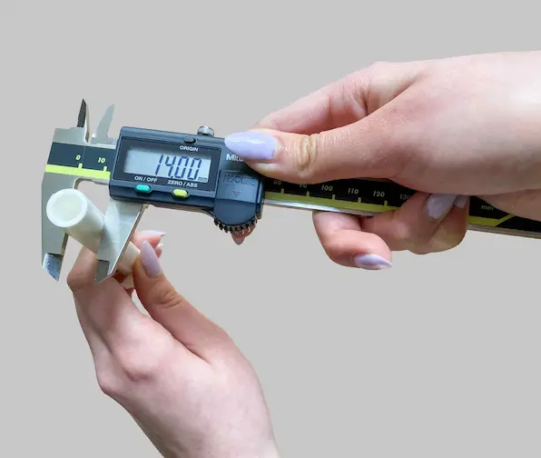 A white tube with a tubing diameter of 14 mm is getting measured with a caliper gauge.