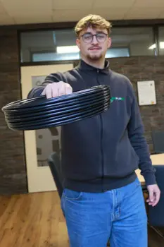 A young man with blond hair holding a ring of regranulated tubing into the camera with one hand