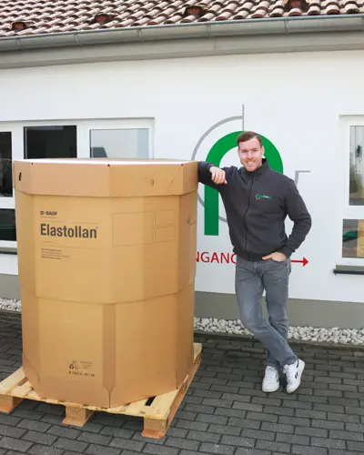 Ein großer Karton mit Granulat für Co2 reduzierten Schlauch. Ein Mann lehnt daran.